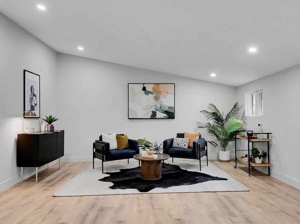 Basement lounge with black armchairs, a cowhide rug, round wood table and palm plant