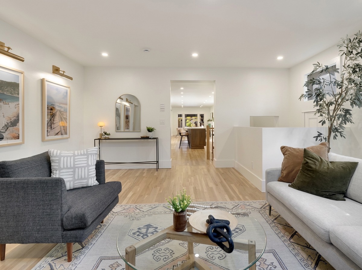 Bright open living room with a charcoal sofa, white sofa, coastal wall art, arched mirror over a console and a potted olive tree