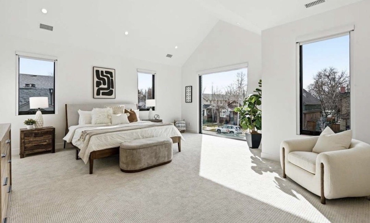 Bright primary bedroom with a vaulted ceiling, upholstered bed, bench and cream accent chair