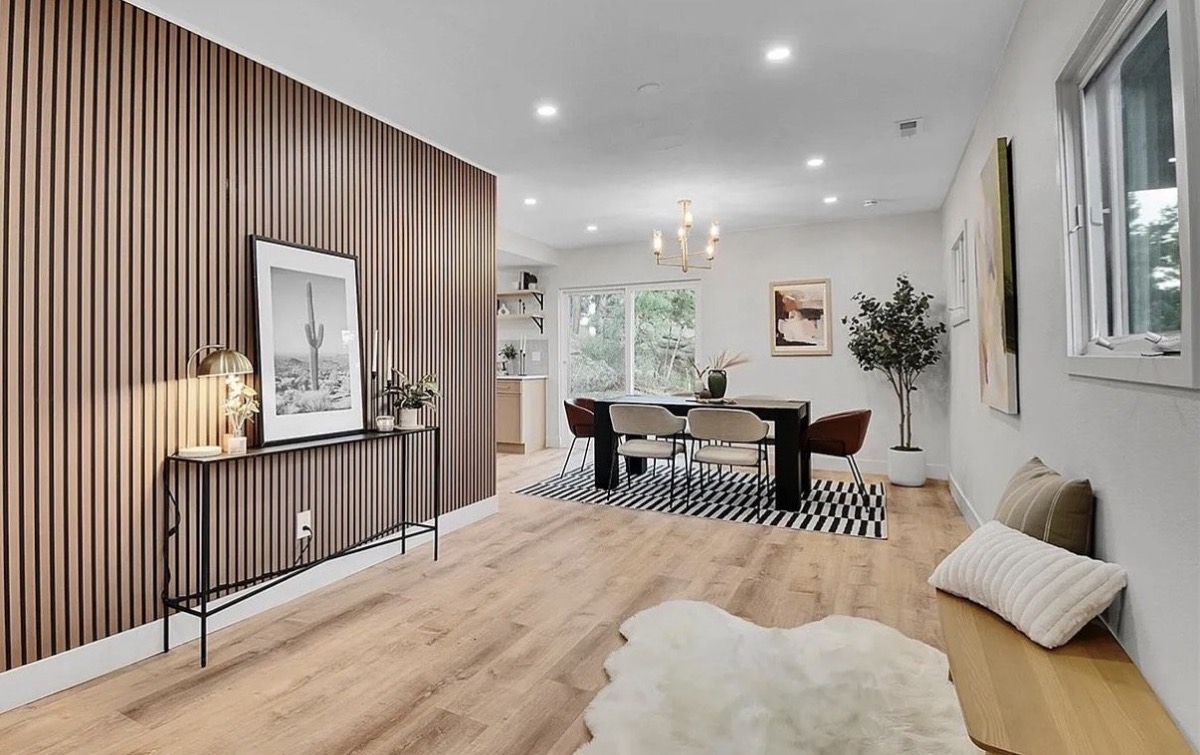 Dining area with a slatted wood accent wall, black table, checkerboard rug and sheepskin throw