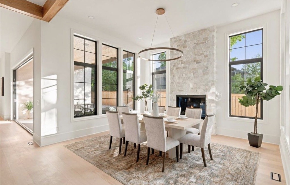 Dining room with a stone fireplace, ring chandelier, cream upholstered chairs and black-framed windows