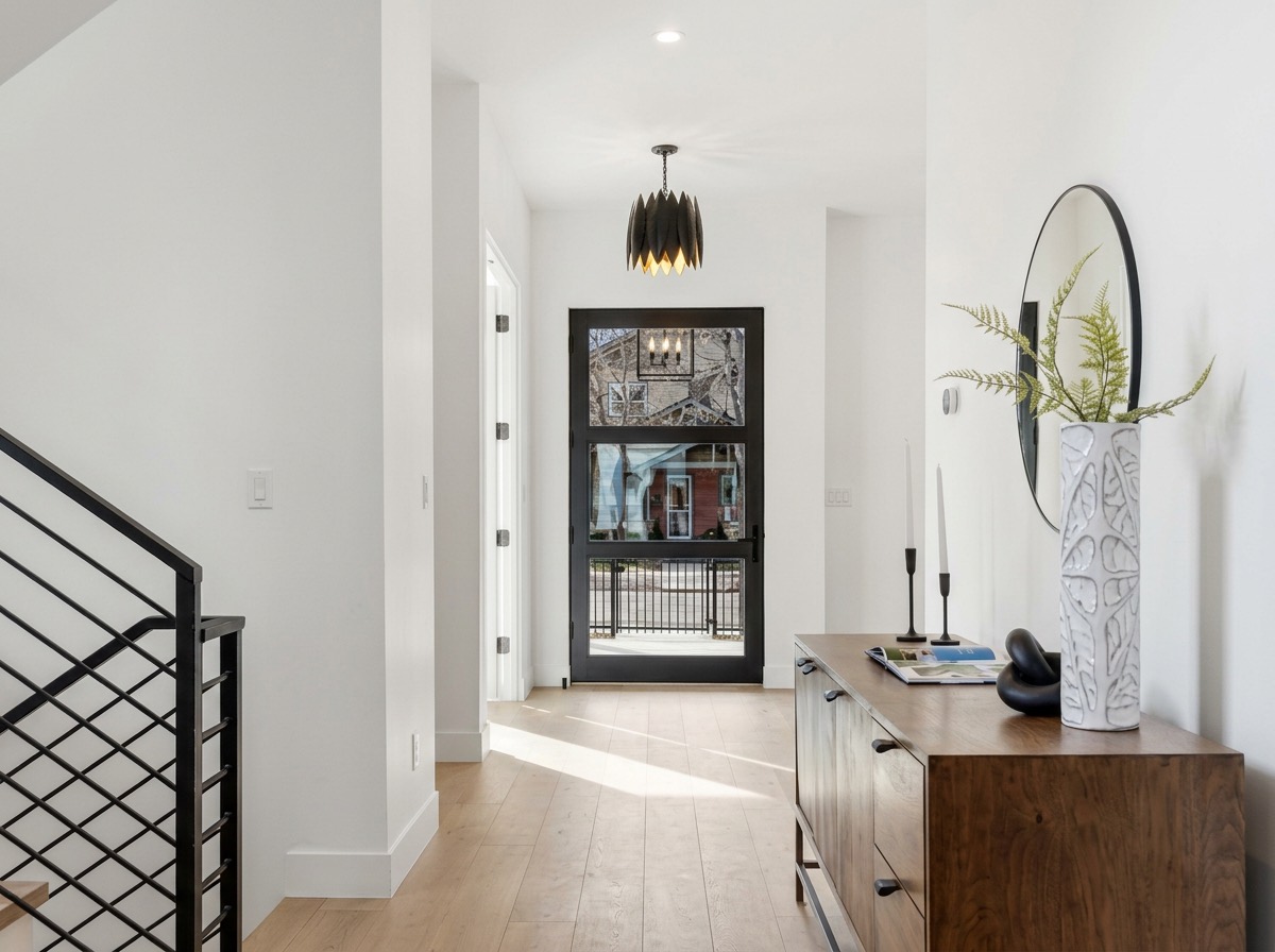 Modern entryway with a black glass front door, sculptural pendant light, walnut console and round mirror