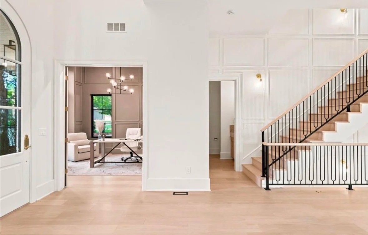 Foyer with a paneled staircase wall, black iron railing and a view into a home office