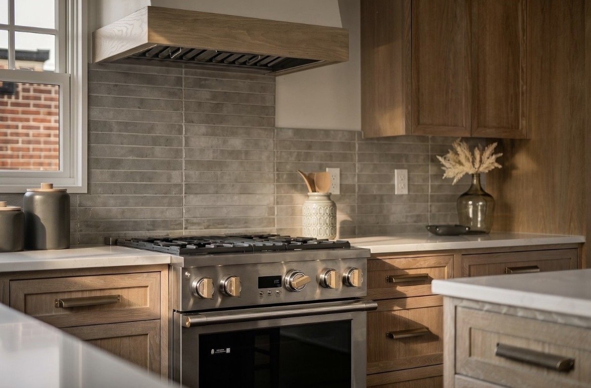 Close-up of a professional range with a gray zellige tile backsplash, white plaster hood and rift oak cabinetry