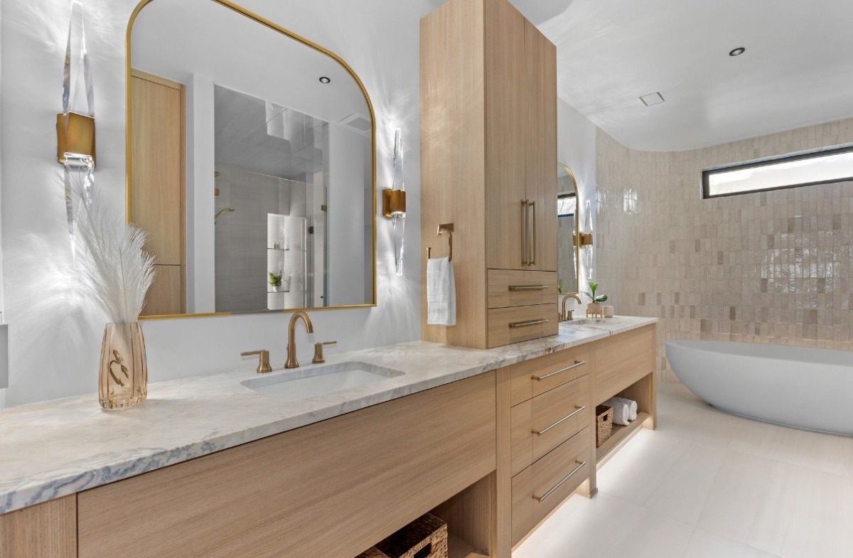 Spa-style bathroom with a floating oak vanity, brass mirror, freestanding tub and textured tile