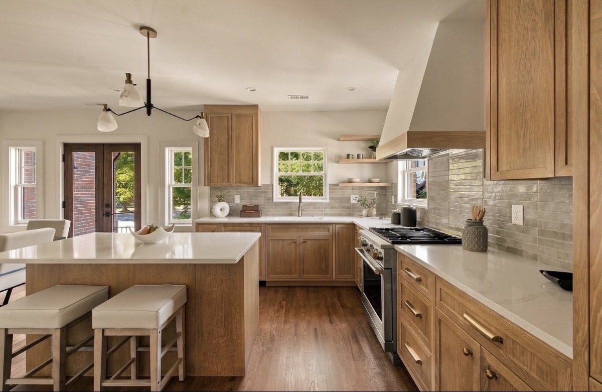 White oak kitchen with a quartz island, cream counter stools, black sputnik pendant and French doors to the yard